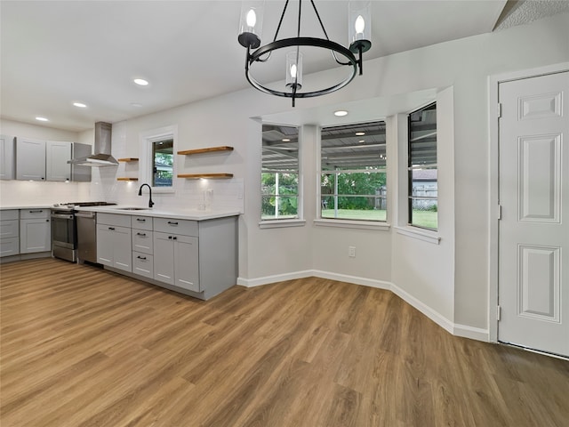 kitchen featuring a chandelier, wall chimney range hood, gray cabinets, stainless steel range, and light wood-type flooring