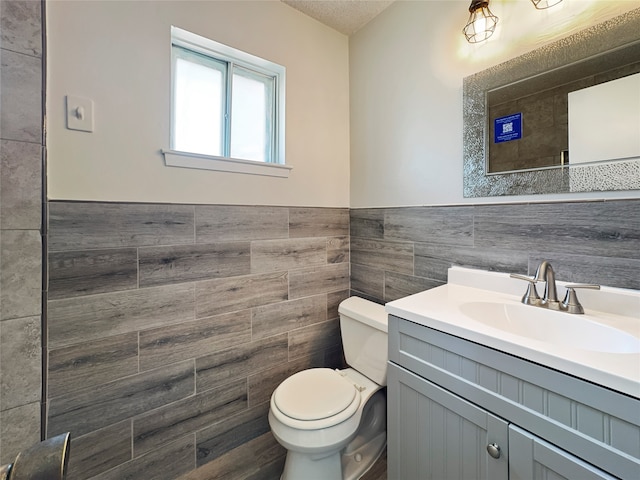 bathroom with toilet, tile walls, vanity, and a textured ceiling