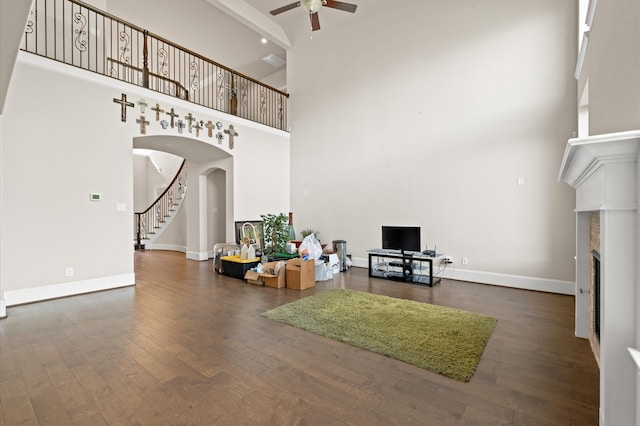 living room featuring ceiling fan, a towering ceiling, and dark wood-type flooring