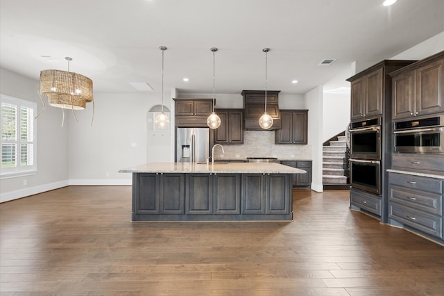 kitchen featuring dark brown cabinets, stainless steel appliances, hanging light fixtures, and an island with sink