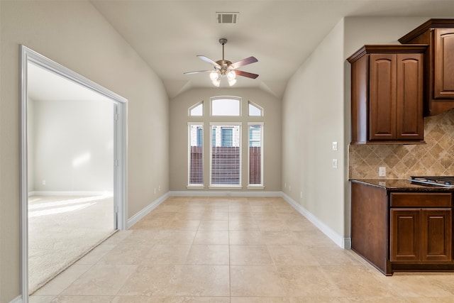 interior space featuring vaulted ceiling, ceiling fan, decorative backsplash, dark stone countertops, and light tile patterned flooring