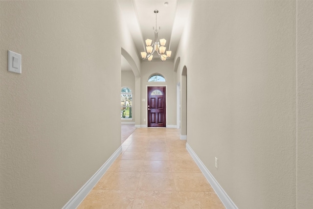 hall featuring arched walkways, light tile patterned floors, baseboards, and an inviting chandelier