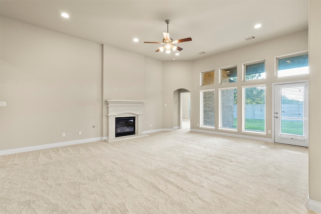 unfurnished living room with a towering ceiling, light colored carpet, and ceiling fan