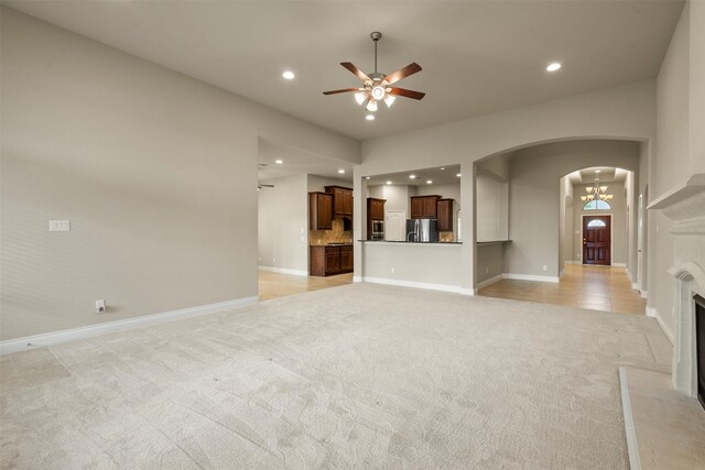 unfurnished living room featuring a tile fireplace, light carpet, and ceiling fan with notable chandelier