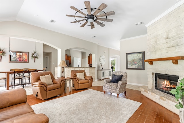 living room with ceiling fan, crown molding, hardwood / wood-style floors, a stone fireplace, and lofted ceiling