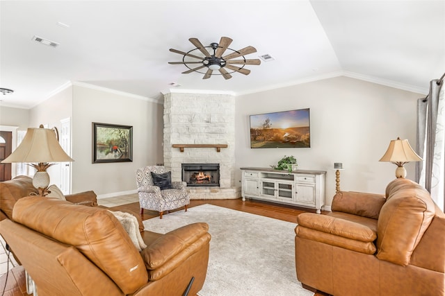 living room with ceiling fan, a stone fireplace, wood-type flooring, vaulted ceiling, and ornamental molding