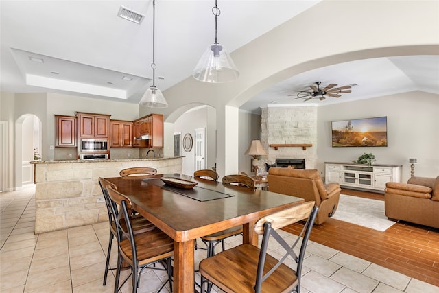 dining space with light wood-type flooring, a tray ceiling, vaulted ceiling, ceiling fan, and a fireplace