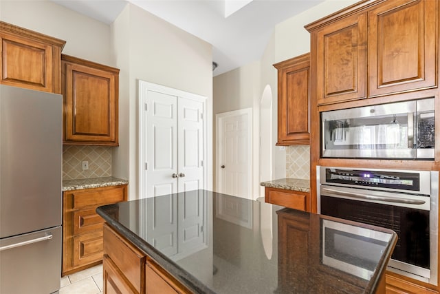 kitchen with decorative backsplash, light tile patterned floors, appliances with stainless steel finishes, and dark stone counters