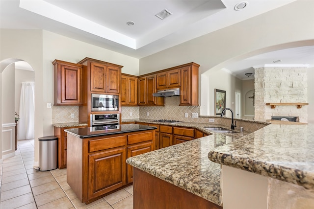 kitchen featuring light stone countertops, appliances with stainless steel finishes, sink, light tile patterned floors, and a center island