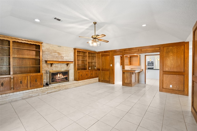 unfurnished living room featuring ceiling fan, built in shelves, light tile patterned floors, a brick fireplace, and vaulted ceiling