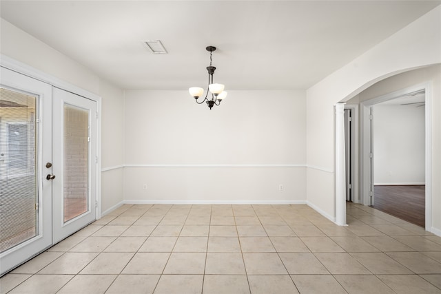 empty room with french doors, a chandelier, and light tile patterned floors