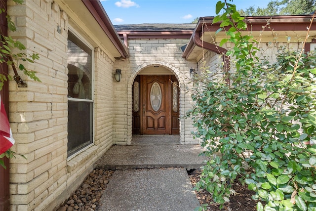 doorway to property with a shingled roof and brick siding