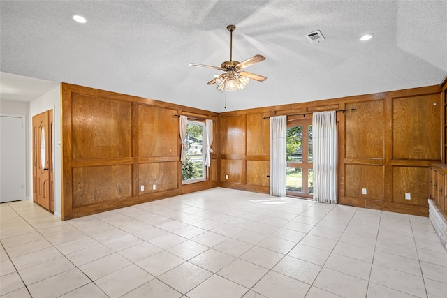 empty room with ceiling fan, a textured ceiling, wooden walls, and light tile patterned flooring