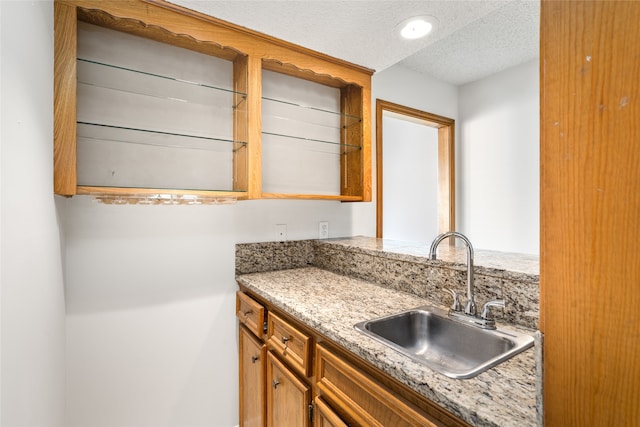 kitchen featuring light stone countertops, sink, and a textured ceiling