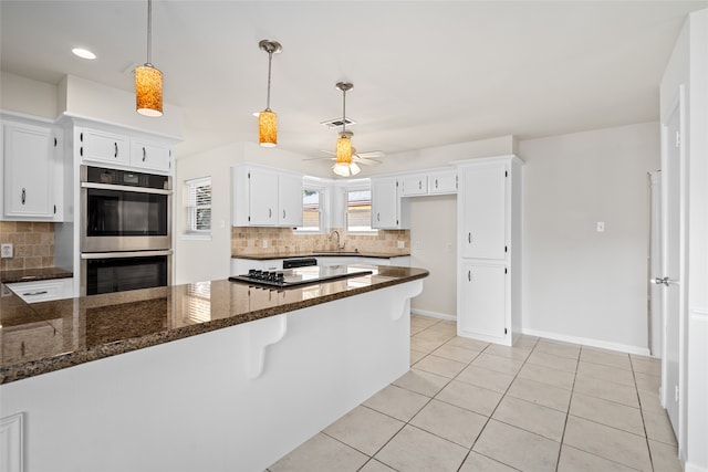 kitchen with double oven, dark stone counters, decorative backsplash, and white cabinets