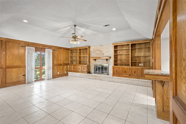 unfurnished living room with ceiling fan, light tile patterned flooring, a textured ceiling, wooden walls, and a fireplace