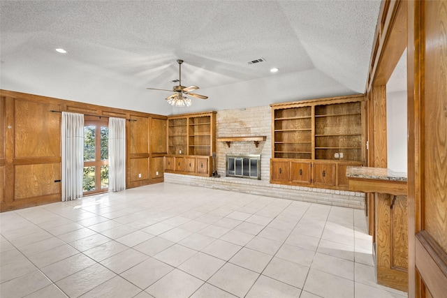 unfurnished living room with built in features, a fireplace, visible vents, wooden walls, and a textured ceiling