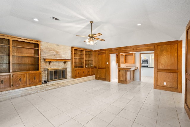 unfurnished living room featuring ceiling fan, a fireplace, built in features, vaulted ceiling, and light tile patterned floors