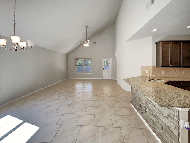 kitchen with ceiling fan with notable chandelier, light stone counters, sink, decorative backsplash, and kitchen peninsula