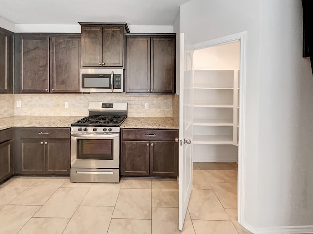 kitchen with dark brown cabinetry, light stone countertops, stainless steel appliances, and tasteful backsplash