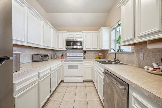 kitchen with sink, appliances with stainless steel finishes, vaulted ceiling, and white cabinets