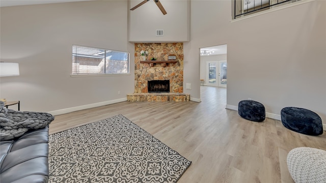 living room with ceiling fan, french doors, a fireplace, a towering ceiling, and light hardwood / wood-style floors