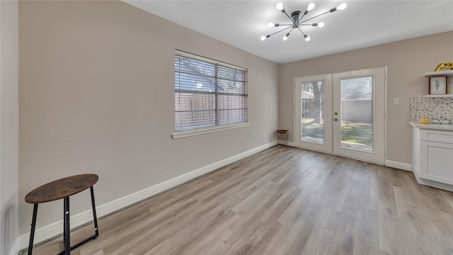 unfurnished dining area with french doors, an inviting chandelier, and light hardwood / wood-style floors