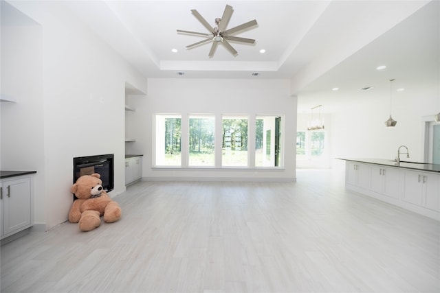 living room with a tray ceiling, sink, ceiling fan with notable chandelier, and light wood-type flooring