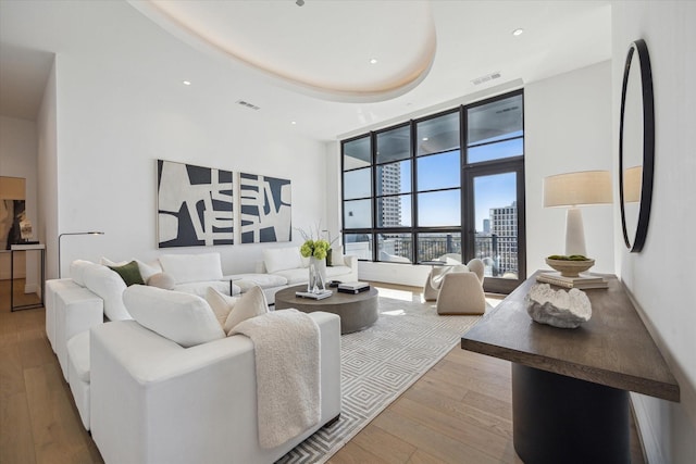 living area with a tray ceiling, hardwood / wood-style floors, a towering ceiling, and visible vents