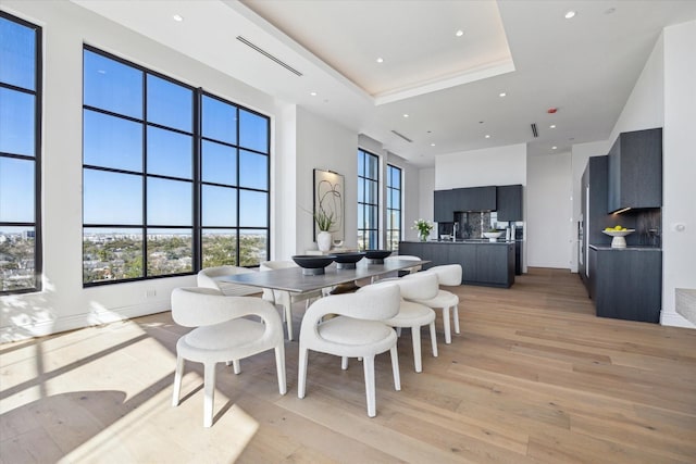 dining room with light wood finished floors, a high ceiling, a tray ceiling, and recessed lighting