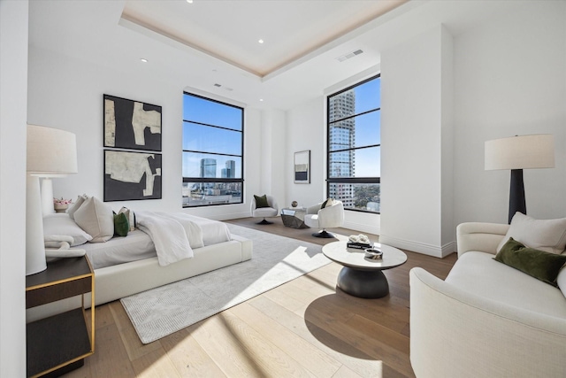 bedroom with baseboards, visible vents, hardwood / wood-style floors, a tray ceiling, and recessed lighting