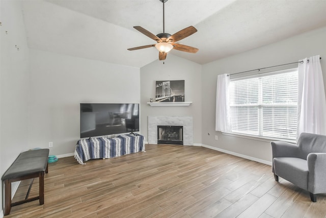 living room featuring ceiling fan, lofted ceiling, a premium fireplace, and hardwood / wood-style floors