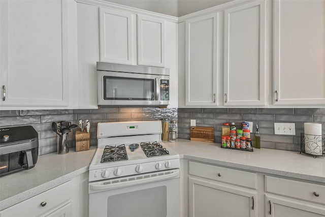 kitchen with white gas stove, decorative backsplash, and white cabinets