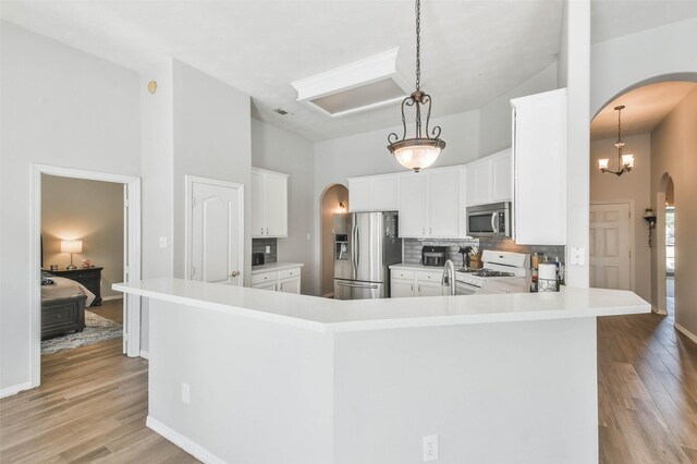 kitchen with white cabinetry, kitchen peninsula, pendant lighting, stainless steel appliances, and backsplash