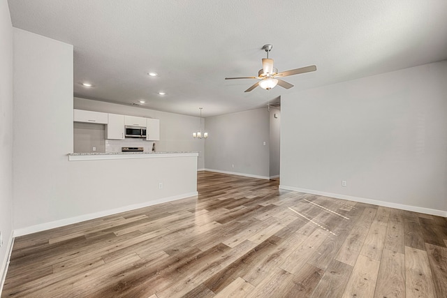 unfurnished living room with ceiling fan with notable chandelier, light wood-type flooring, and a textured ceiling