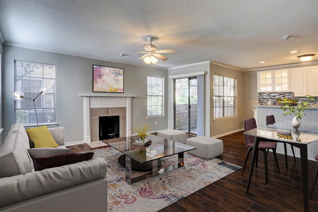 living room with ceiling fan, ornamental molding, a tiled fireplace, and dark hardwood / wood-style flooring