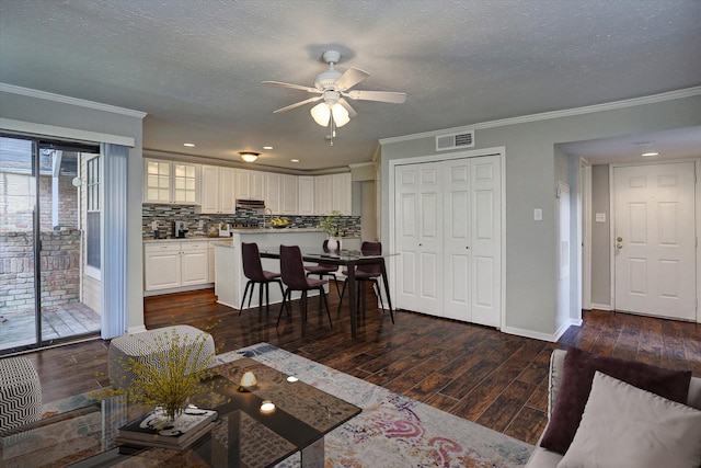 living room with crown molding, ceiling fan, visible vents, and dark wood-type flooring