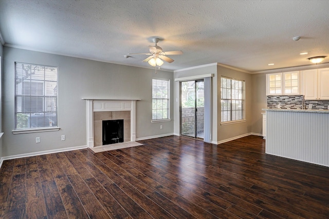 unfurnished living room featuring dark wood-type flooring, ornamental molding, a textured ceiling, and a tile fireplace