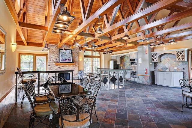 dining area featuring vaulted ceiling with beams, stone tile floors, wood ceiling, and a brick fireplace