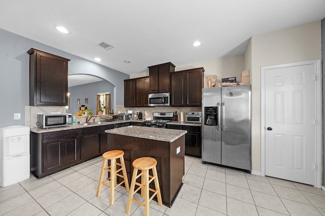 kitchen with tasteful backsplash, a center island, a kitchen breakfast bar, stainless steel appliances, and light tile patterned floors