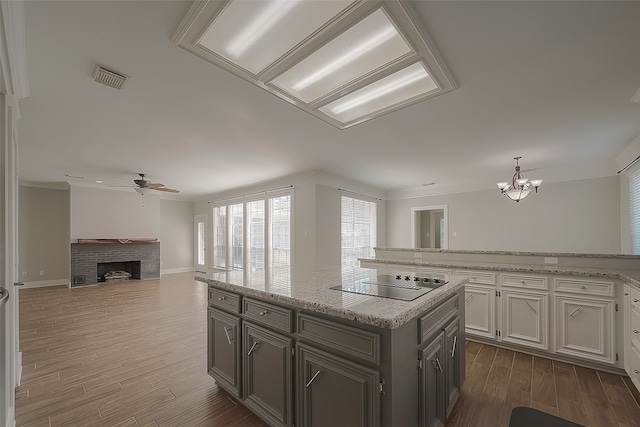 kitchen featuring a kitchen island, a brick fireplace, dark wood-type flooring, black electric stovetop, and crown molding