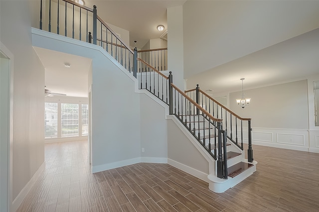 stairs with ceiling fan with notable chandelier, hardwood / wood-style flooring, and high vaulted ceiling