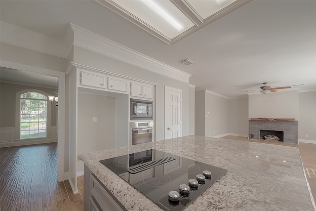 kitchen with a brick fireplace, light stone counters, wood-type flooring, stainless steel appliances, and white cabinetry