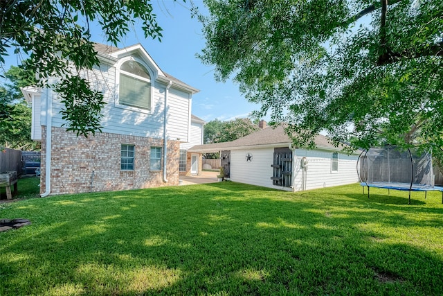 rear view of property featuring a trampoline, a patio area, and a lawn