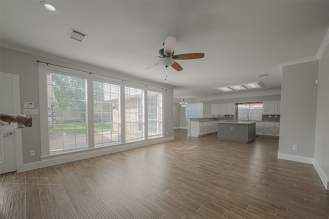 unfurnished living room with ceiling fan with notable chandelier, crown molding, hardwood / wood-style floors, and sink