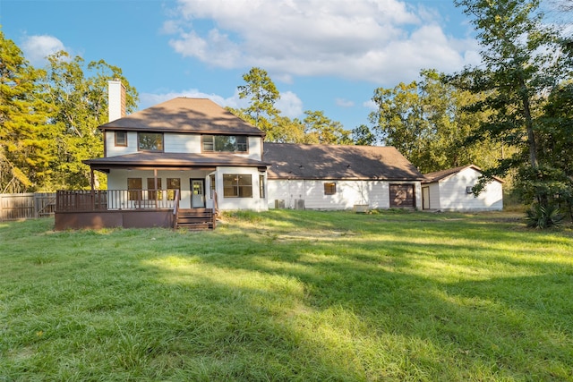 back of property with a garage, a wooden deck, a yard, and an outbuilding