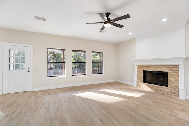 unfurnished living room featuring a healthy amount of sunlight, a tiled fireplace, light wood-type flooring, and ceiling fan