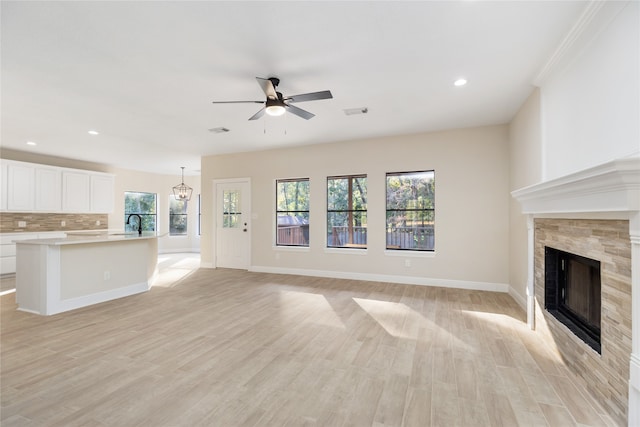 unfurnished living room with a tiled fireplace, light hardwood / wood-style floors, plenty of natural light, and ceiling fan with notable chandelier