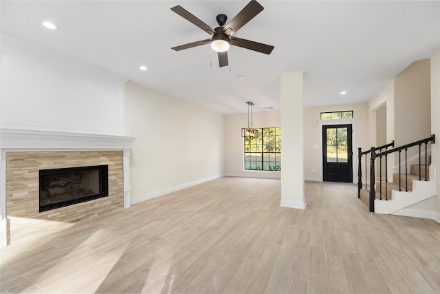 unfurnished living room with light hardwood / wood-style flooring, a tile fireplace, and ceiling fan with notable chandelier