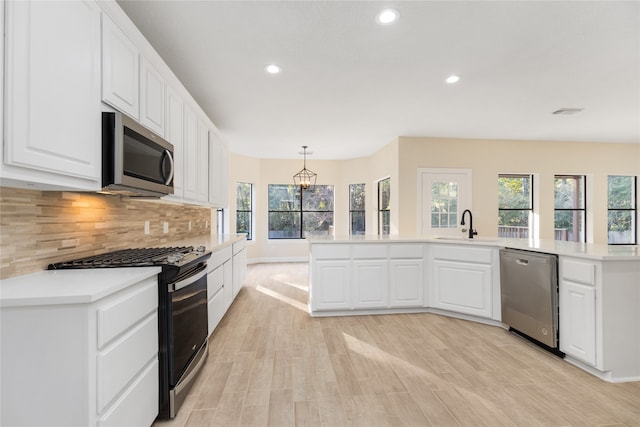 kitchen featuring appliances with stainless steel finishes, hanging light fixtures, light hardwood / wood-style floors, white cabinets, and decorative backsplash